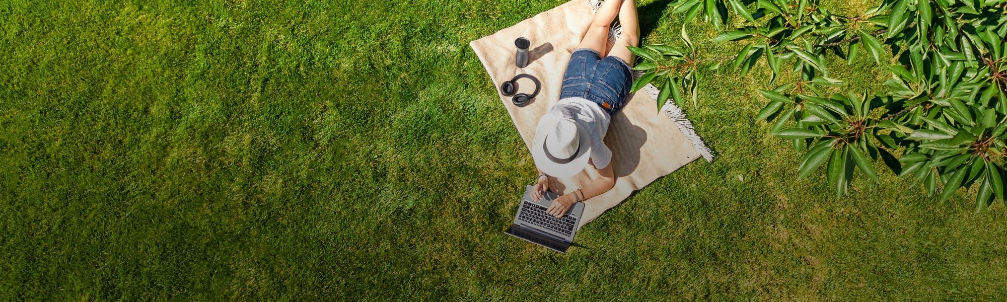 woman in a hat on a blanket outside with a laptop